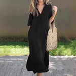 Stylish black maxi dress with pockets, worn by a woman holding a beige woven tote bag, against a green grass background.