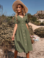 Stylish woman in olive green midi dress and straw hat strolling through natural setting