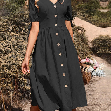 Elegant beige midi dress with a v-neck, button-down closure, and short puff sleeves, worn by a woman holding a basket of flowers in a scenic outdoor setting.