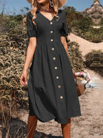 Elegant black button-down midi dress with puff sleeves, styled with a sun hat and basket of flowers in a lush, natural setting.