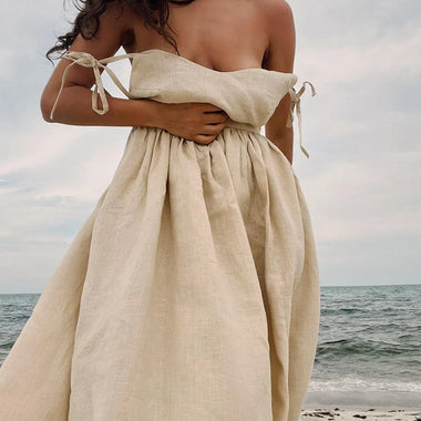 Elegantes Sommerstrandkleid aus Baumwolle mit V-Ausschnitt und luftigen Trägern in natürlichen Tönen vor malerischer Meerkulisse