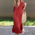 Fashionable red cotton linen dress, loose fit with V-neck and short sleeves, accompanied by a chic straw handbag, set against a green lawn backdrop.