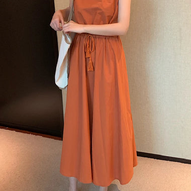 Vibrant orange women's summer dress with short sleeves, mid-length skirt, and tassel detail at waist, worn with white sneakers