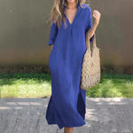 Vibrant blue cotton linen dress, featuring a v-neck and short sleeves, worn with a beige woven tote bag, styled in a casual yet fashionable outdoor setting.