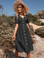 A stylish woman in a black, button-down summer dress with a wide-brimmed hat, standing in a scenic desert landscape.