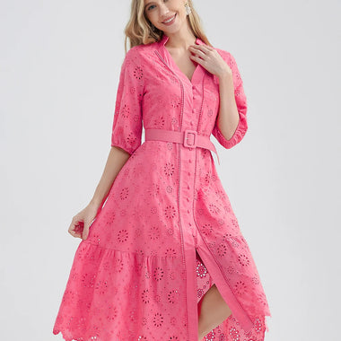 Elegant pink cotton dress with delicate eyelet embroidery, featuring a collared neckline, front button closure, and tiered ruffled skirt. The model is smiling and standing comfortably in the image, showcasing the dress's flattering A-line silhouette.