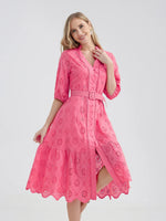 Bright pink cotton dress with delicate embroidered floral pattern, flared skirt, and belted waist on a smiling young woman.