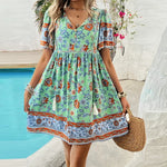 Vibrant floral-patterned summer dress with puff sleeves, v-neck, and ruffled skirt worn by a woman standing near a swimming pool.