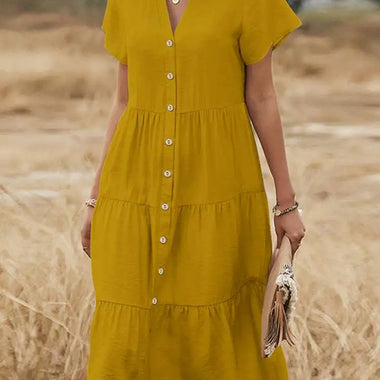 Elegant beige linen dress with V-neck, short sleeves, and tiered skirt, worn in a wheat field setting.