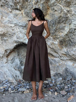 Elegantes braunes Sommerkleid einer attraktiven Dame vor einer Steinwand. Dieses lässige Baumwollkleid mit V-Ausschnitt und A-Linie Silhouette verleiht der Trägerin einen sophistizierten und femininen Look.