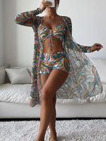 Colorful two-piece swimsuit with matching cover-up, featuring tie-front design and bold abstract patterns, showcased against a white sofa backdrop.