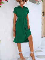 Elegant green linen summer dress with waist tie, worn by a smiling woman with sunglasses in a floral setting.