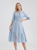 Elegant blue women's dress with floral embroidery, belted waistline, and mid-length sleeves, worn by a smiling young woman with blonde hair against a white background.