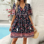 Floral print short dress with v-neck, bell sleeves, and cinched waist, worn by a young woman standing by a swimming pool surrounded by greenery and trees.